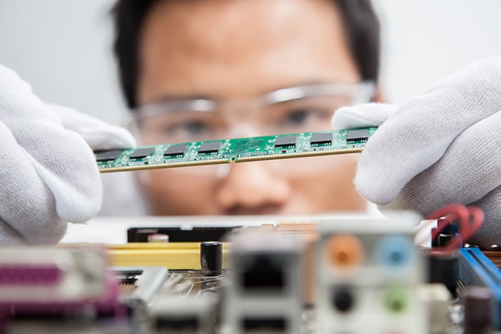 Close up of circuit board being inspected by an engineer in white gloves and safety glasses