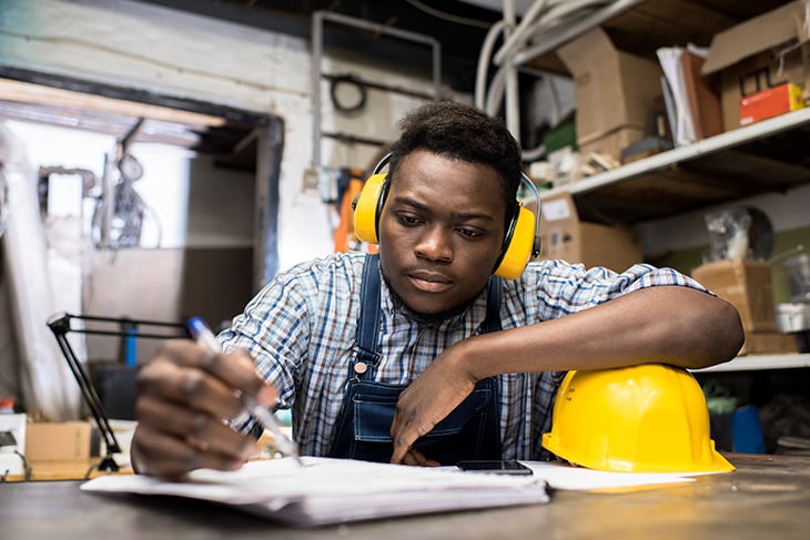 Young African-American man seated at a table doing paperwork in a factory setting